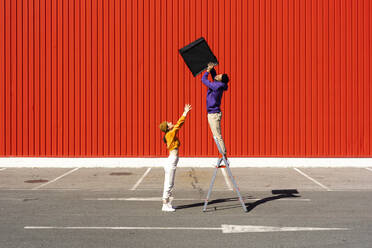 Young man and woman performing with a box in front of a red wall - ERRF02852