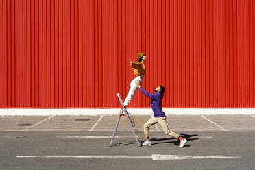 Young man and woman performing with a ladder in front of a red wall - ERRF02857