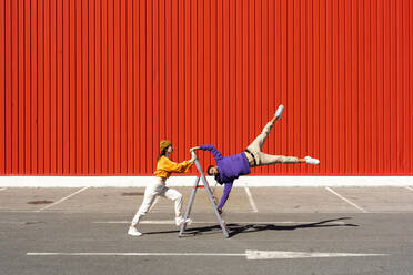 Young man and woman performing with a ladder in front of a red wall - ERRF02859