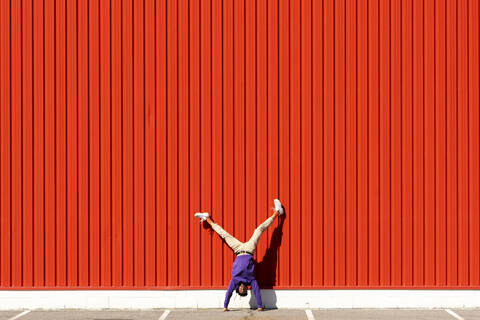 Junger Mann macht einen Handstand an einer roten Wand, lizenzfreies Stockfoto