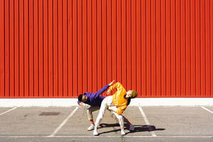 Young man and woman performing in front of a red wall - ERRF02870