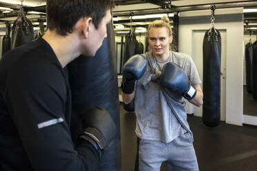 Trainer und Boxerin beim Training am Sandsack im Fitnessstudio - VPIF02068