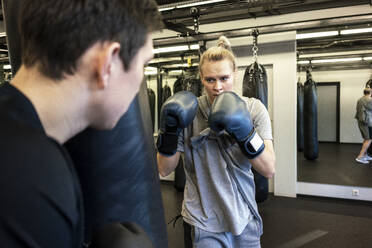 Coach and female boxer practising at sandbag in gym - VPIF02069