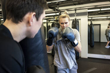 Trainer und Boxerin beim Training am Sandsack im Fitnessstudio - VPIF02069