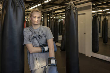 Porträt einer Frau mit Boxhandschuhen am Sandsack im Fitnessstudio - VPIF02072