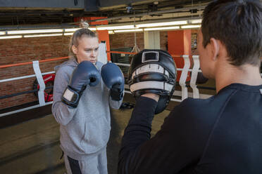 Weibliche Boxerin beim Sparring mit ihrem Trainer im Fitnessstudio - VPIF02084