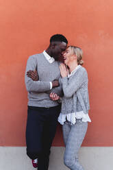 Happy affectionate young couple standing at an orange wall - FMOF00873