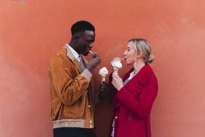 Junges Paar steht an einer orangefarbenen Wand und isst Eiscreme - FMOF00874