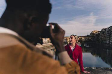 Junger Mann fotografiert seine Freundin auf einer Brücke über dem Fluss Arno, Florenz, Italien - FMOF00877