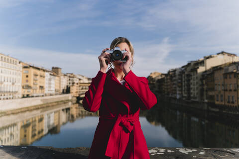 Junge Frau beim Fotografieren auf einer Brücke über dem Fluss Arno, Florenz, Italien, lizenzfreies Stockfoto