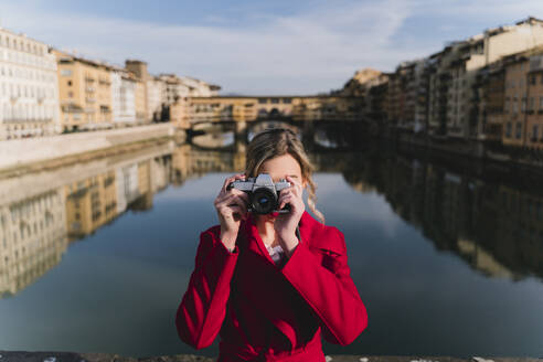 Young woman taking a picture on a bridge above river Arno, Florence, Italy - FMOF00880