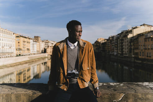 Junger Mann mit einer Kamera auf einer Brücke über den Arno, Florenz, Italien - FMOF00884