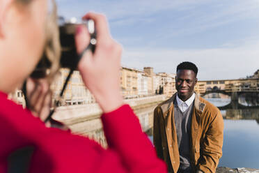 Junge Frau, die ein Foto von ihrem Freund auf einer Brücke über dem Arno macht, Florenz, Italien - FMOF00886