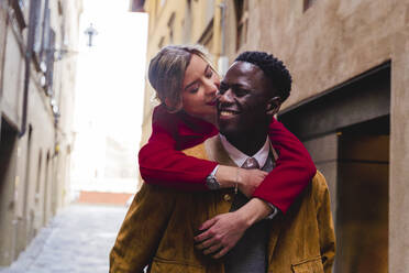 Happy young man carrying girlfriend piggyback in an alley in the city of Florence, Italy - FMOF00890