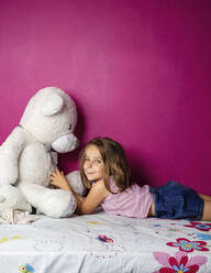Porträt eines kleinen Mädchens mit großem Teddybär vor einer rosa Wand - LJF01373