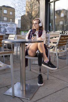 Young woman with leg prosthesis sitting in a sidewalk cafe in the city - FBAF01283