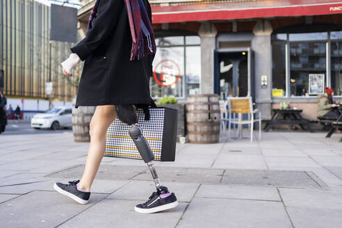 Low section of woman with leg prosthesis walking in the city - FBAF01284