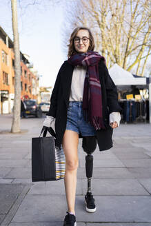 Portrait of confident young woman with leg prosthesis walking in the city - FBAF01287