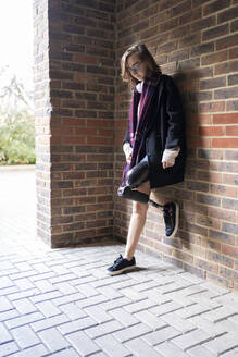 Young woman with leg prosthesis standing at a brick wall - FBAF01288