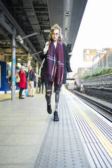 Young woman with leg prosthesis walking at station platfom - FBAF01299