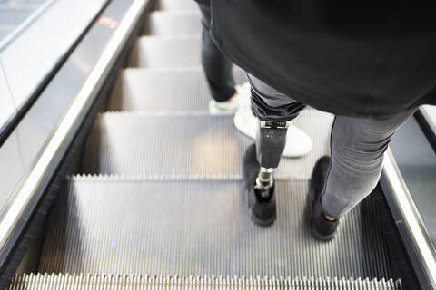 Close-up of woman with leg prosthesis standing on escalator stock photo