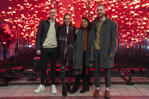 Portrait of happy friends in front of red light bulbs - FBAF01313