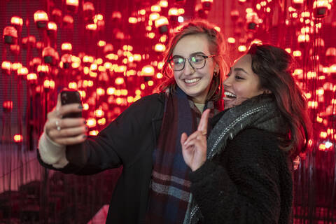 Portrait of happy friends taking a selfie in front of red light bulbs stock photo