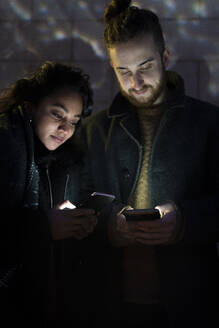 Couple looking at illuminated smartphones in the dark - FBAF01315