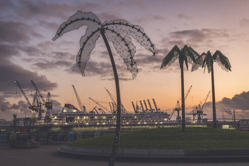 Deutschland, Hamburg, Künstliche Palmen im Sankt-Pauli-Park in der Abenddämmerung mit kommerziellem Dock im Hintergrund - KEBF01475