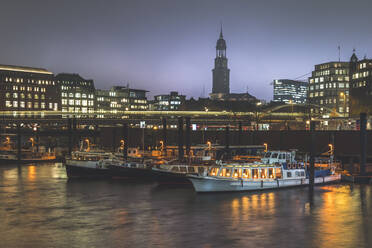 Deutschland, Hamburg, Boote vertäut im Stadthafen in der Abenddämmerung mit Lichtweg und Turm der St. Michaelskirche im Hintergrund - KEBF01479