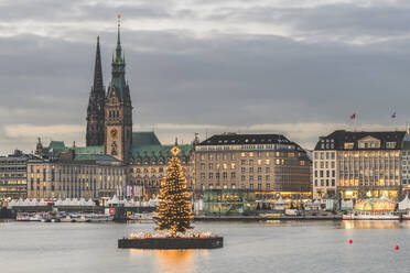 Germany, Hamburg, Illuminated Alstertanne tree at dusk with Jungfernstieg promenade and Saint Nicholas Church in background - KEBF01487