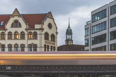 Deutschland, Hamburg, Unscharfe Bewegung einer Hochbahn, die an einem Wohnhaus vorbeifährt, mit dem Turm der St. Michaelskirche im Hintergrund - KEBF01493