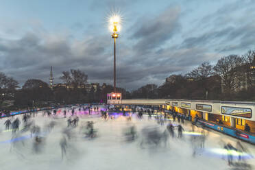Germany, Hamburg, People ice-skating in Planten un Blomen park at dusk - KEBF01494