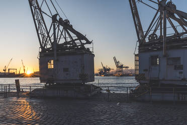 Deutschland, Hamburg, Alte Hafenkräne am Elbufer bei Sonnenuntergang - KEBF01498