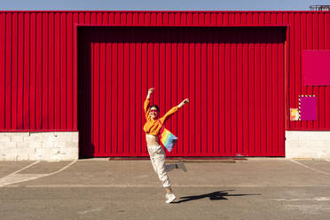 Lesbian with colorful shopping bag in front of a red wall - ERRF02874