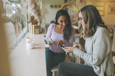 Zwei Frauen benutzen Smartphones in einem Café - CMSF00111