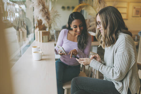 Zwei Frauen benutzen Smartphones in einem Café - CMSF00111