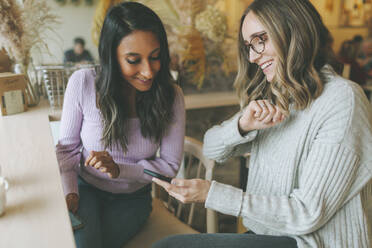 Two women using smartphone in a cafe - CMSF00113