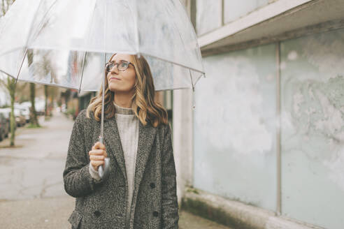 Blonde Frau geht im Regen mit einem Regenschirm - CMSF00119