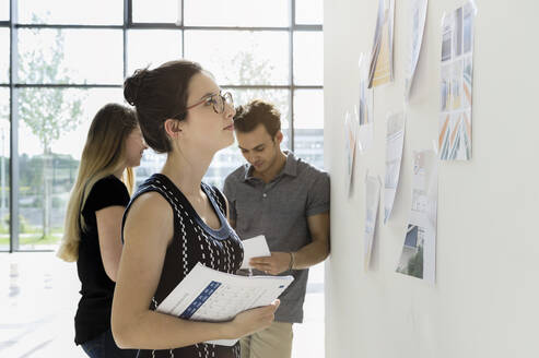 Drei junge Architekten stehen an einem Whiteboard und diskutieren über Entwurfsideen. - CUF54857