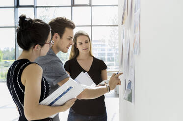 Drei junge Architekten stehen an einem Whiteboard und diskutieren über Entwurfsideen. - CUF54859