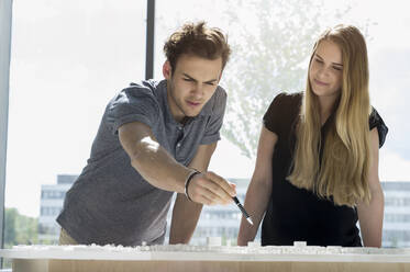 Two young architects standing at a table, working on an architectural model. - CUF54863