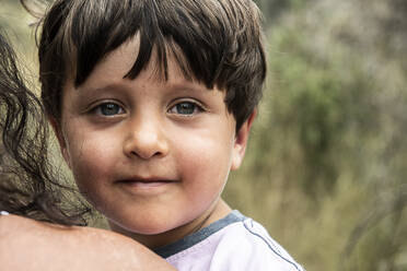 Porträt eines kleinen Jungen mit braunem Haar, der von seiner Mutter getragen wird und in die Kamera schaut. - CUF54893