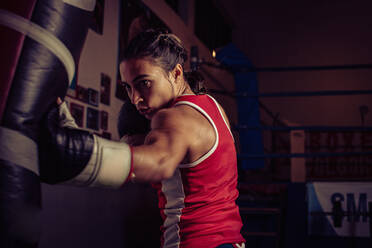 Weibliche Boxerin mit rotem Oberteil trainiert im Fitnessstudio und schlägt auf den Sandsack. - CUF54916