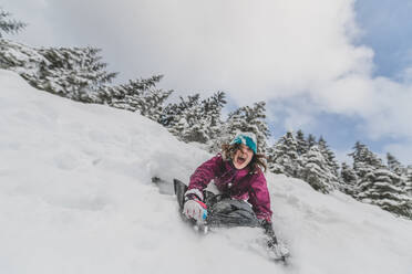 Eine Frau rutscht einen schneebedeckten Abhang in einem kanadischen Wald hinunter. - ISF23977