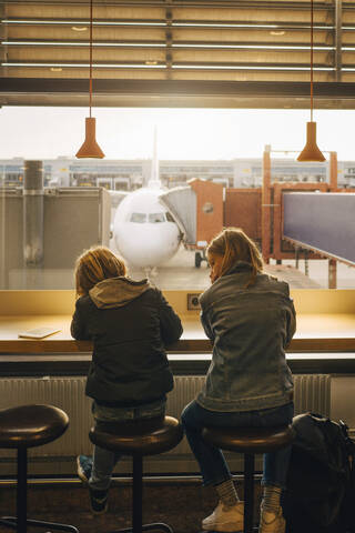 Rückansicht von Bruder und Schwester, die am Flughafen am Fenster sitzen, lizenzfreies Stockfoto