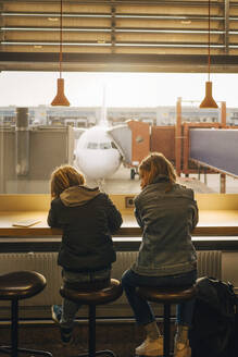 Rückansicht von Bruder und Schwester, die am Flughafen am Fenster sitzen - MASF16776
