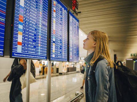 Seitenansicht eines Mädchens, das die Abflugtafel am Flughafen betrachtet, lizenzfreies Stockfoto