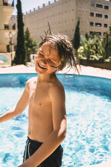 Lächelnder Junge ohne Hemd am Swimmingpool in einem Ferienort - MASF16785