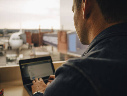 Rückansicht eines reifen Mannes, der im Sitzen am Flughafen einen Laptop benutzt - MASF16791